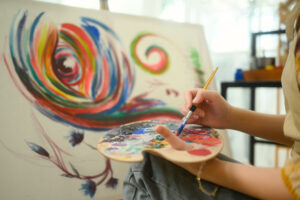 Close up of female artist mixing paint on a palette while working on her painting in studio